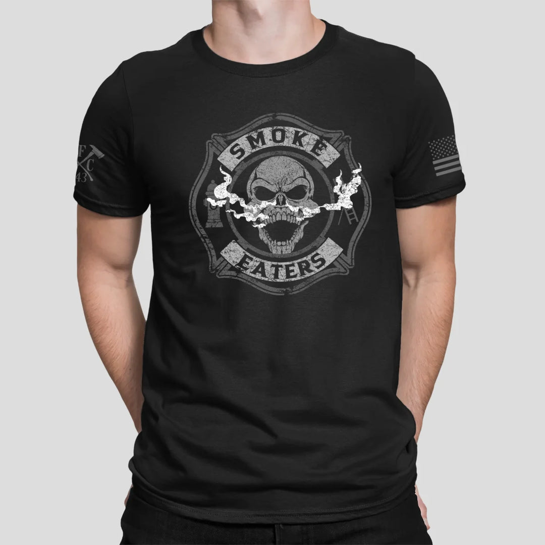 a man wearing a black firefighter t-shirt in black color featuring full-front design of a skull inhaling smoke, with a distressed grey and off-white look.