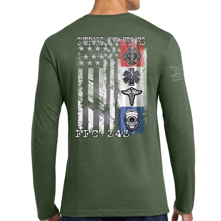 A man wearing a long-sleeve green t-shirt, viewed from the back. The shirt features a large graphic print on the back with a distressed American flag, military-style emblems, and the text 'SUPPORT OUR HEROES' and 'FFC 343'. #color_military-green