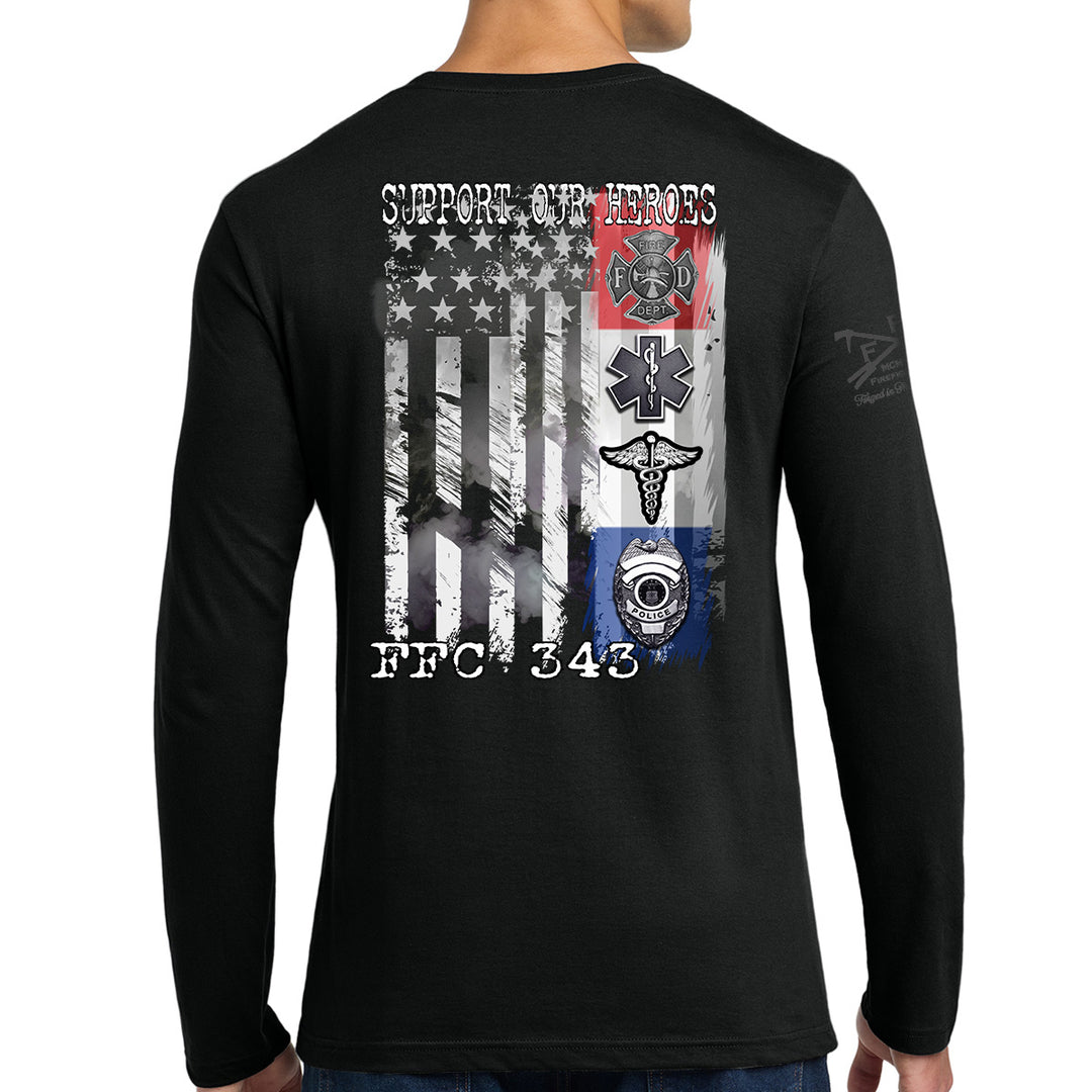 A man wearing a black long-sleeve t-shirt, viewed from the back. The shirt features a large graphic print on the back with a distressed American flag, military-style emblems, and the text 'SUPPORT OUR HEROES' and 'FFC 343'. #color_black