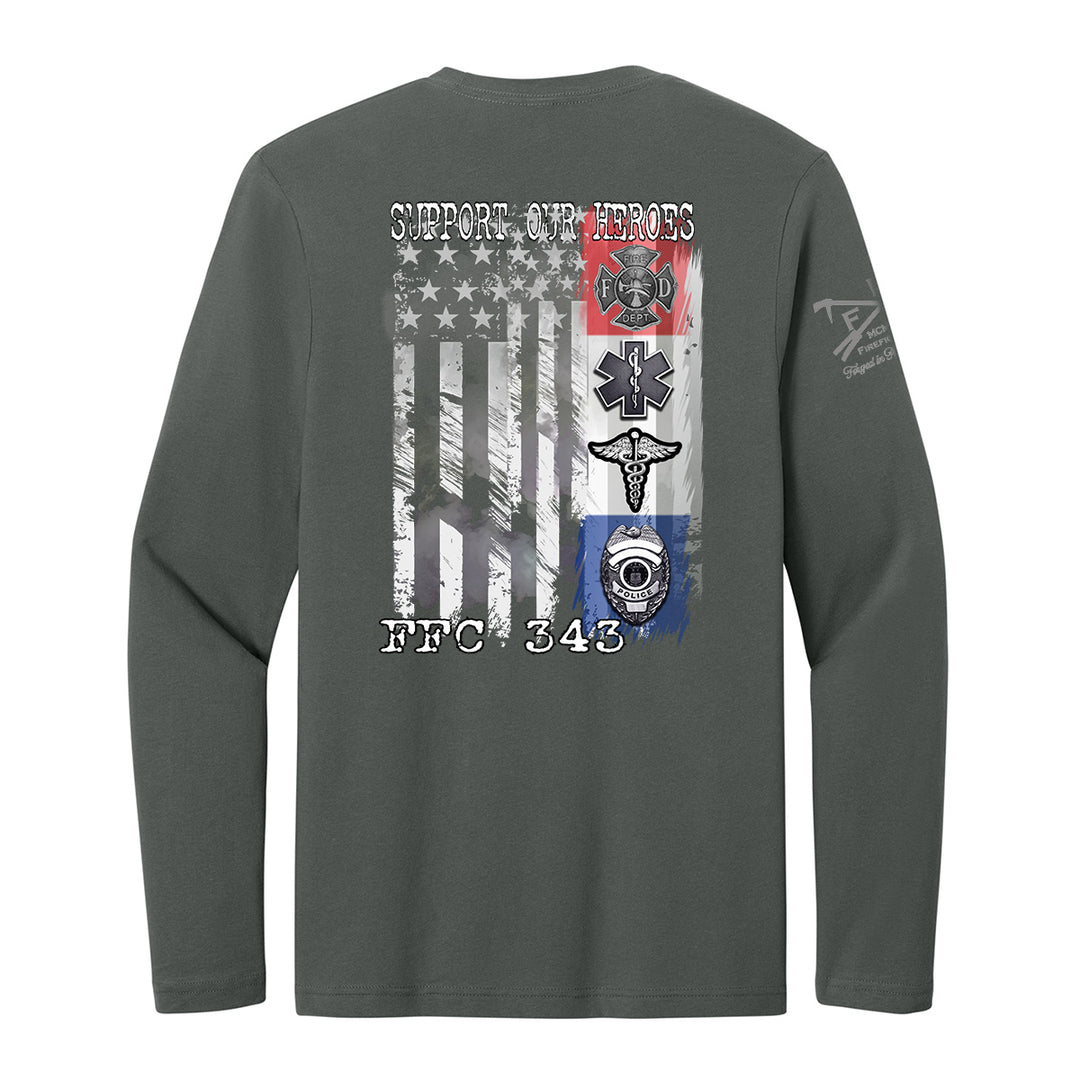 A dark gray long-sleeve t-shirt shown from the back, featuring a large graphic print of a distressed American flag with military and emergency services symbols, including a firefighter helmet, EMT star, and ambulance cross. The text 'SUPPORT OUR HEROES' is printed above the flag, and 'FBC 343' is printed below. #color_charcoal