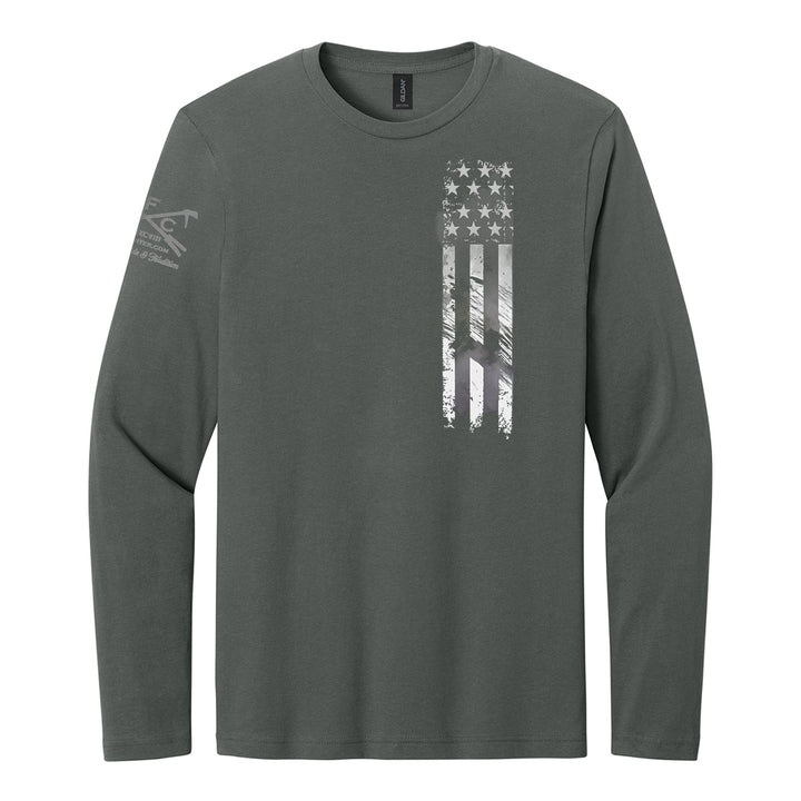 A dark gray long-sleeve t-shirt with a distressed vertical American flag graphic on the left chest and a subtle logo on the right sleeve, shown on a plain white background. #color_charcoal
