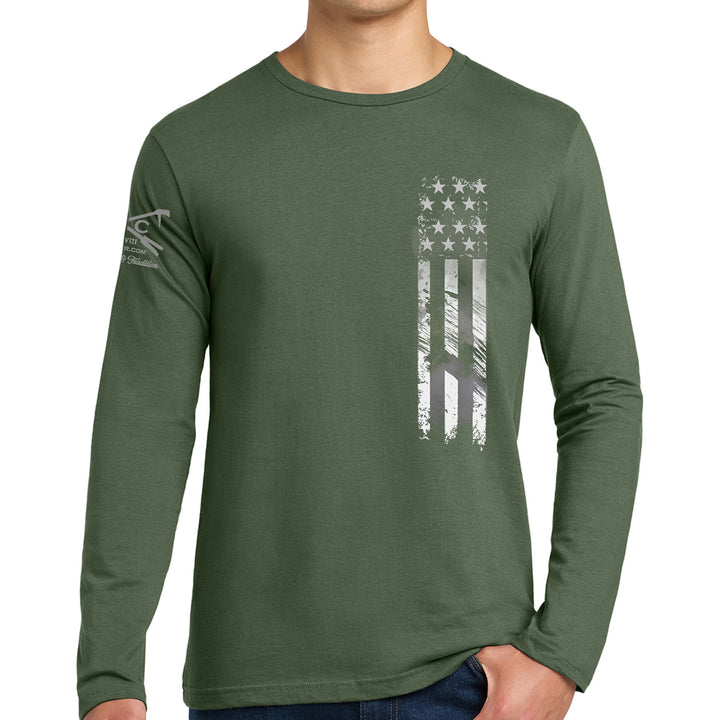 A man wearing a dark olive green long-sleeve t-shirt with a distressed vertical American flag graphic on the chest and a small logo on the left sleeve, set against a plain white background. #color_military-green