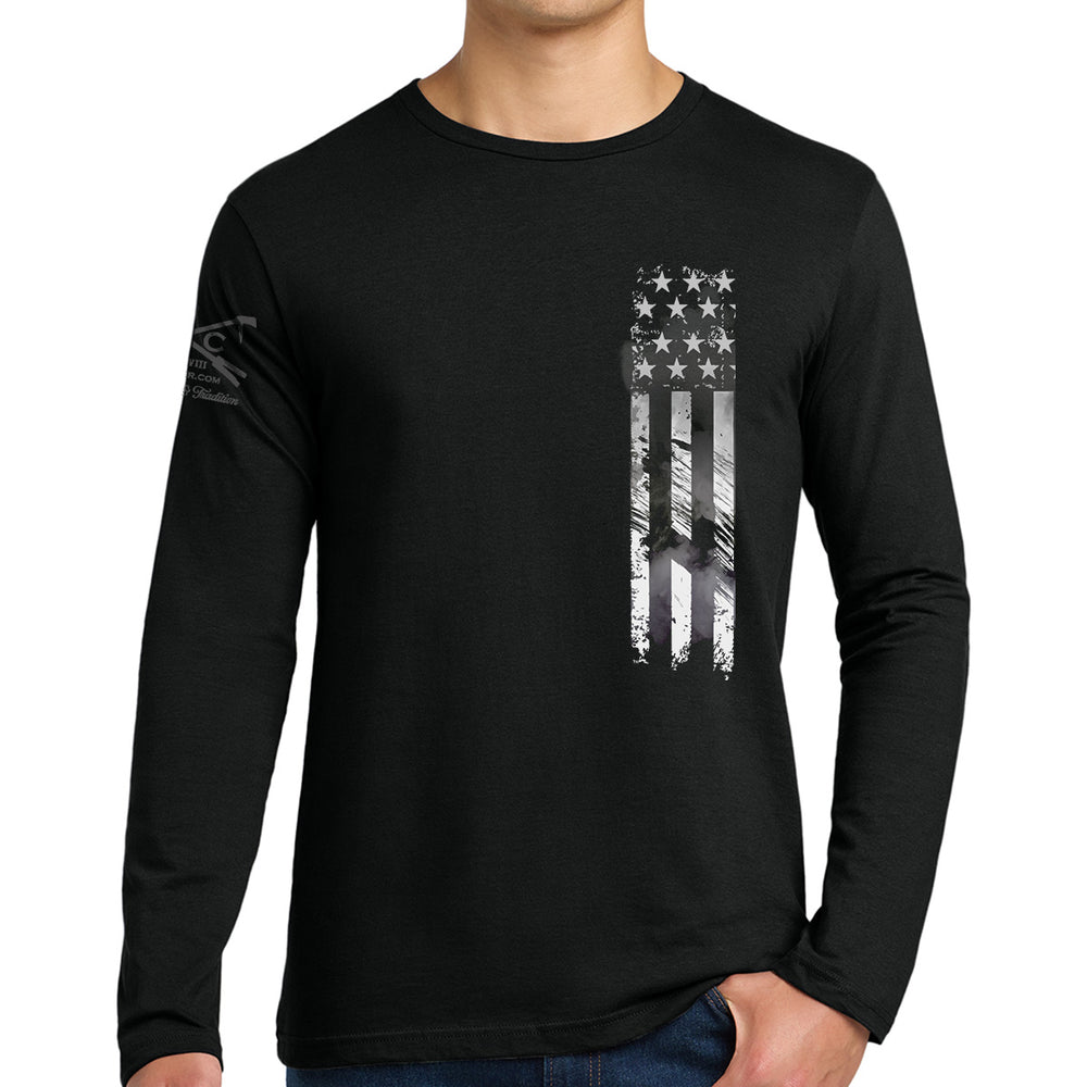 A man wearing a black long-sleeve t-shirt with a distressed vertical American flag graphic in white and gray on the left chest, shown against a plain white background. #color_black