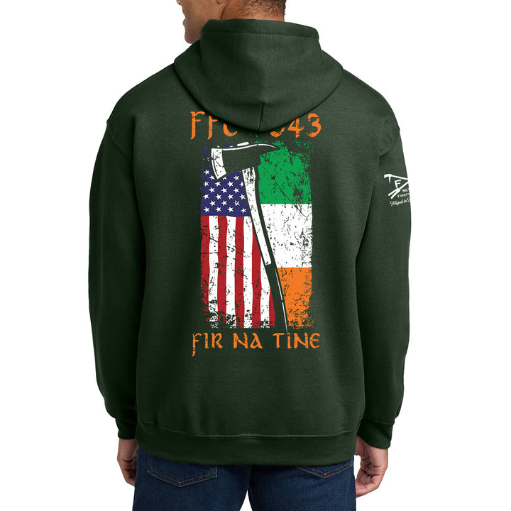 A man wearing a dark green hoodie, viewed from the back. The hoodie features a graphic print of an American flag and an Irish flag with a scythe, along with the text 'FIR 043' and 'FIR NA TINE'. #color_forest-green