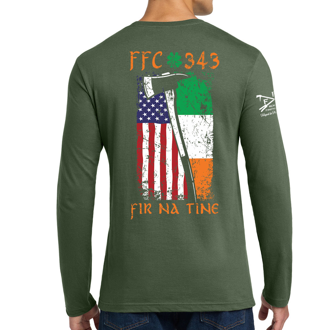 A man wearing a forest green long-sleeve t-shirt, viewed from the back. The shirt features a large graphic print on the back with the text 'FFC 343' and 'FIR NA TINE' in orange, surrounding a distressed graphic of the American flag and an axe, with the Irish tricolor. #color_military-green