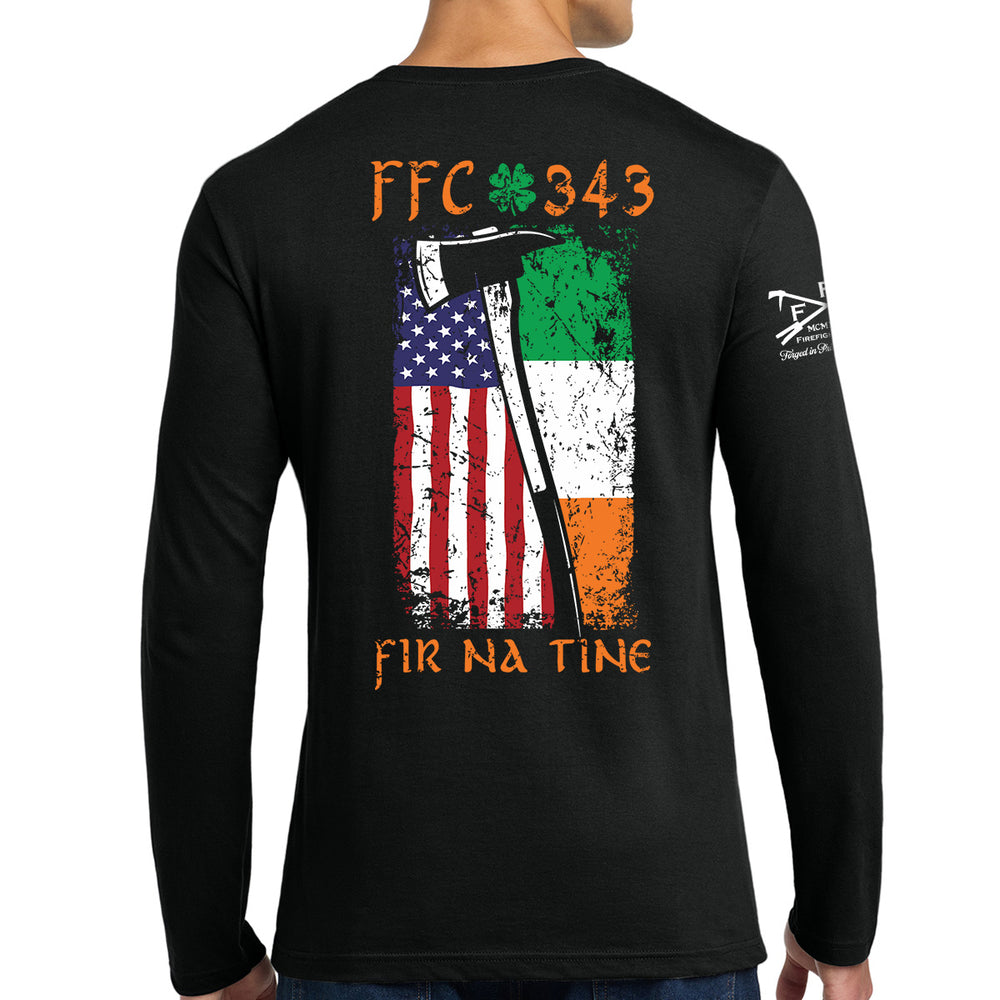 A man wearing a black long-sleeve t-shirt, viewed from the back. The shirt features a large graphic print on the back with the text 'FFC 343' and 'FIR NA TINE' in orange, a green shamrock, and a distressed American and Irish flag design with an axe. #color_black