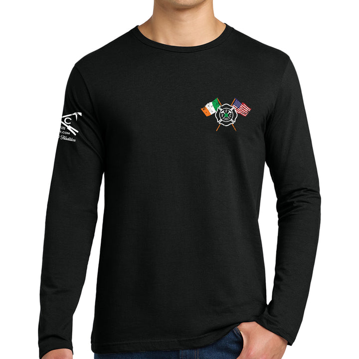 A man wearing a black long-sleeve t-shirt with a small graphic on the left chest featuring crossed flags (Irish flag, American flag, and a green shamrock) and a white graphic on the right sleeve. #color_black
