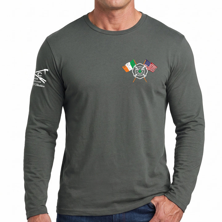 A man wearing a dark gray long-sleeve t-shirt with a small chest graphic of crossed flags (Irish flag, fire department flag, US flag) and a white logo on the left sleeve, set against a plain white background. #color_charcoal