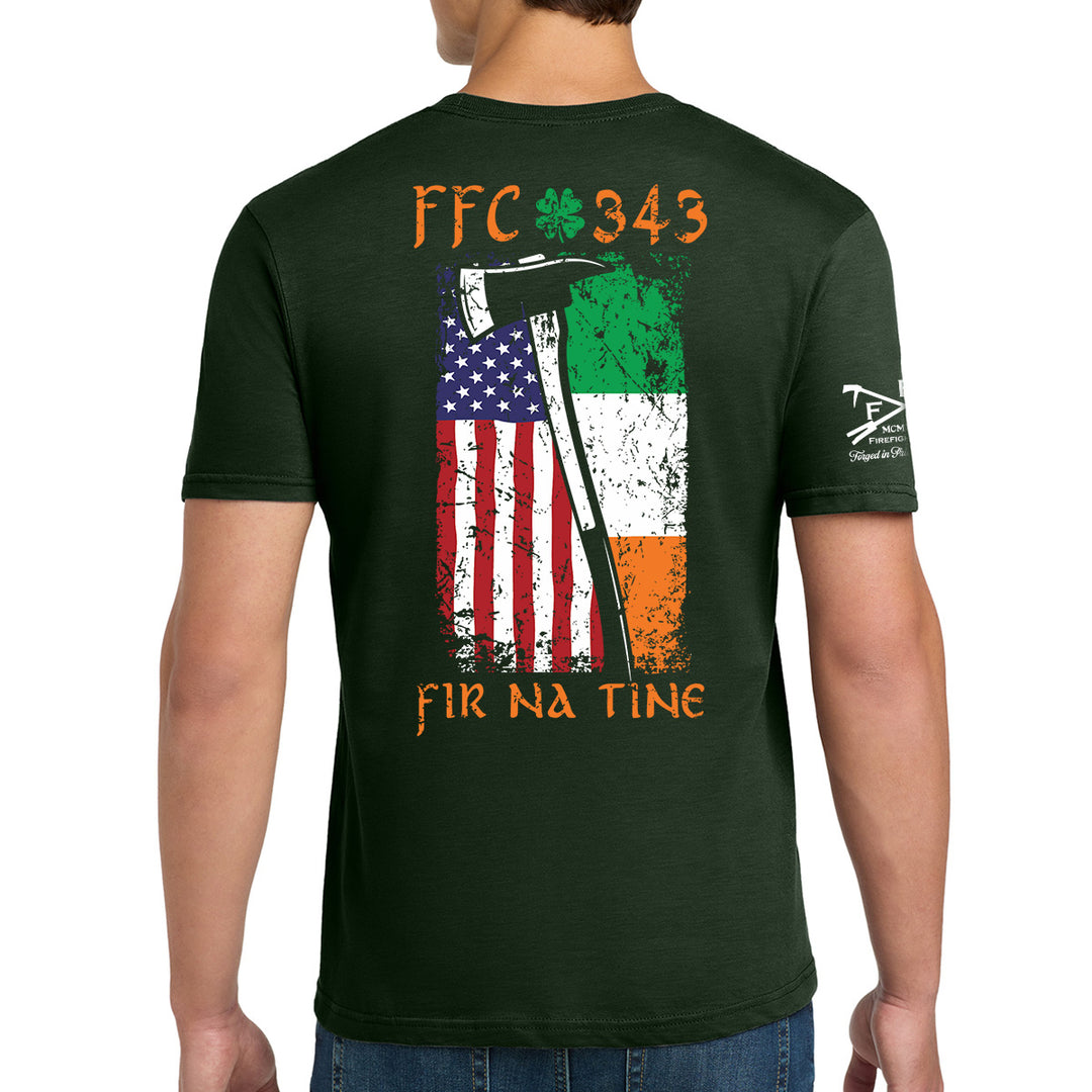 A man wearing a dark green t-shirt, viewed from the back. The shirt features a distressed graphic of the Irish flag and the American flag with an axe, along with the text 'FFC 343' and 'FIR NA TINe'. #color_forest-green