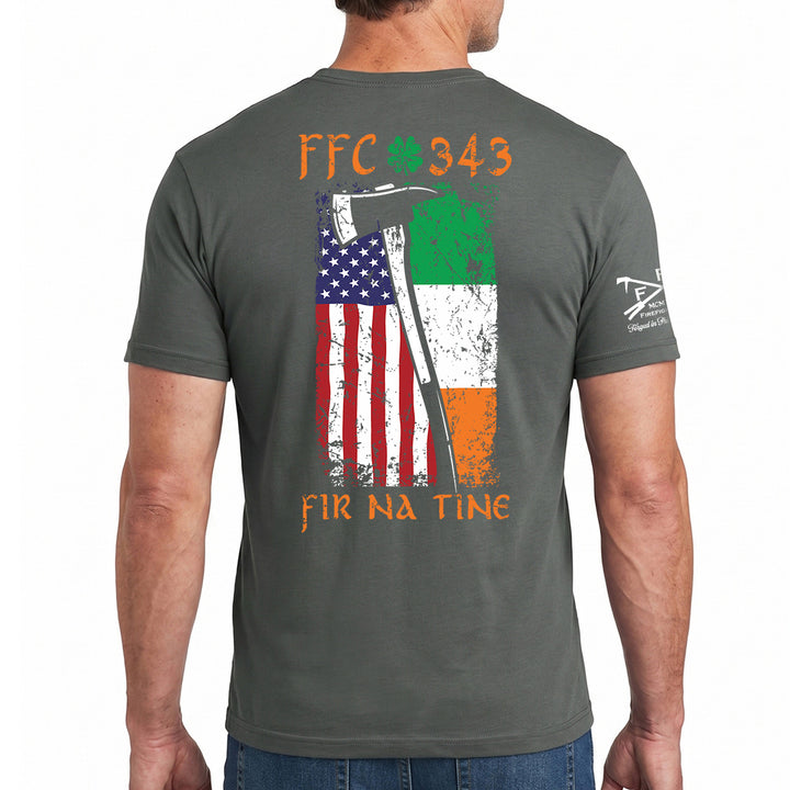 A man wearing a dark gray t-shirt, viewed from the back. The shirt features a distressed graphic of the American flag and the Irish flag with an axe, along with the text 'FFC 343' and 'FIR NA TINE'. #color_charcoal