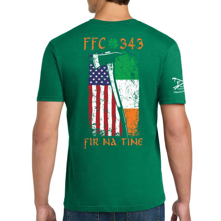 A man wearing a green t-shirt, viewed from the back. The shirt features a distressed graphic of the Irish flag and the American flag with an axe, along with the text 'FFC 343' and 'FIR NA TINE'. #color_kelly-green