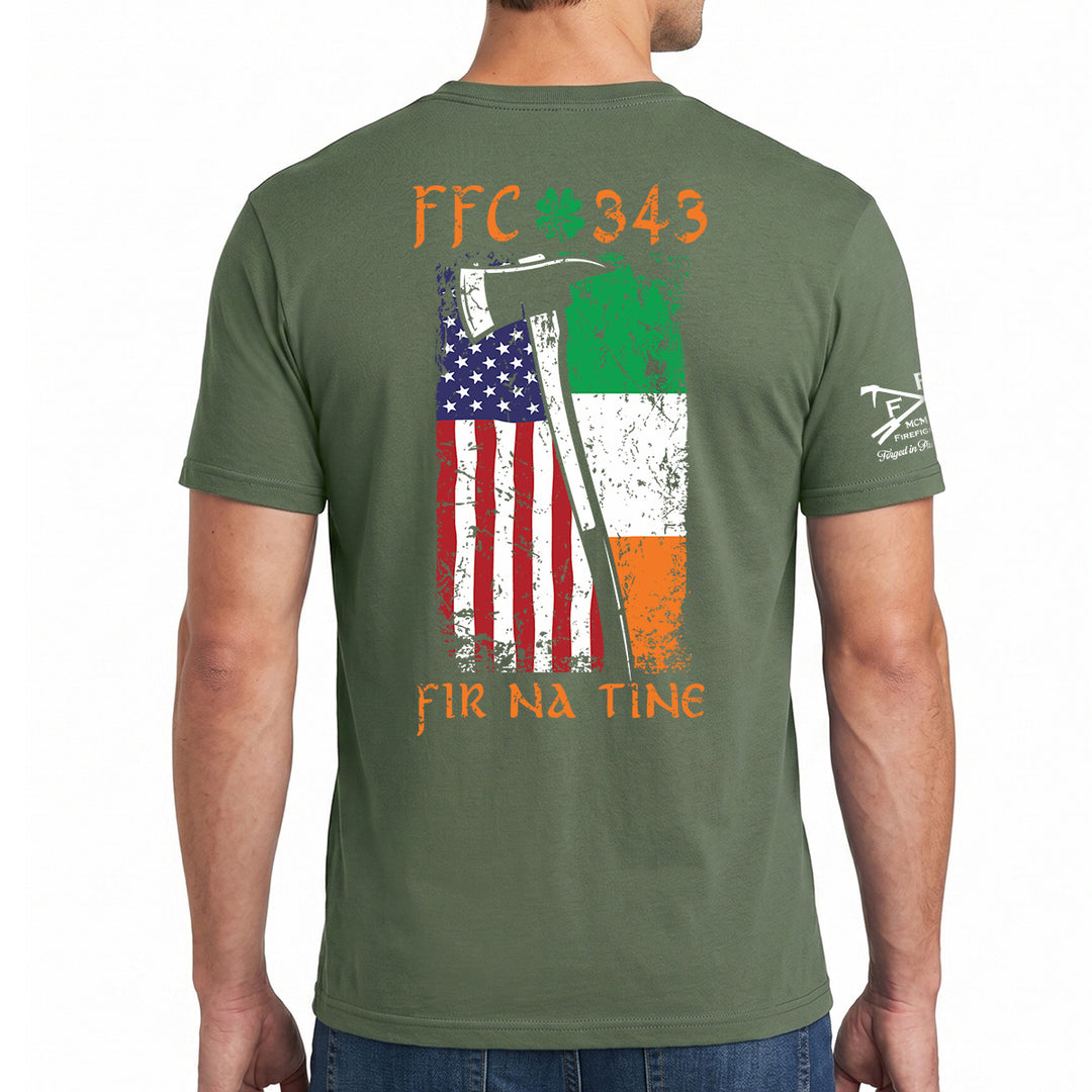 A man wearing an olive green t-shirt, viewed from the back. The shirt features a distressed graphic of the Irish flag and the American flag with an axe, along with the text 'FFC 343' and 'FIR NA TINe'. #color_military-green