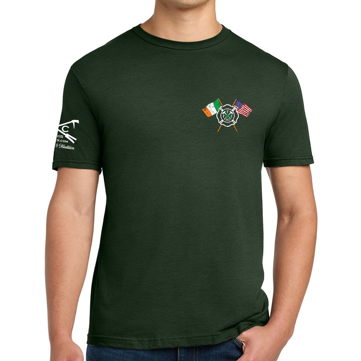 A man wearing a dark forest green t-shirt. The shirt features a small graphic on the left chest with crossed flags (Irish flag, American flag, and a fire department helmet) and a white graphic on the right sleeve. #color_forest-green