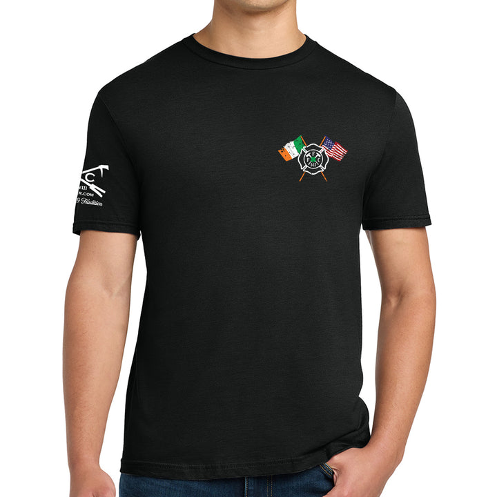 A man wearing a black short-sleeve t-shirt with a small graphic on the left chest featuring crossed firefighter helmets and flags, and a white graphic on the right sleeve. #color_black