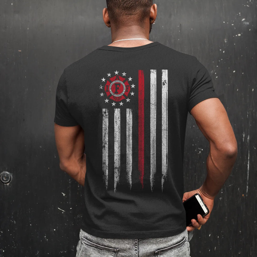 A man wearing a black IAFF firefighter T-shirt with a full back design print of an IAFF Thin Red Line Flag, a distressed American flag with the IAFF logo 