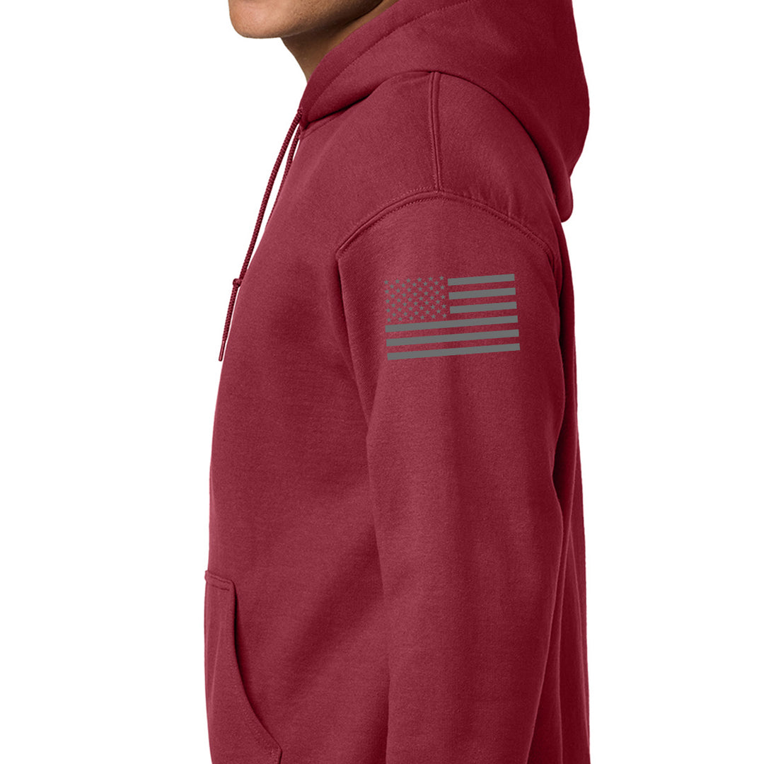 A close-up side view of a person wearing a heathered burgundy pullover hoodie with a gray American flag graphic printed on the upper left sleeve, against a plain white background. #color_cardinal-red
