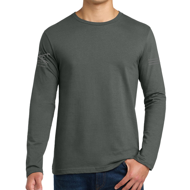 A man wearing a dark gray long-sleeve crewneck shirt with a subtle distressed American flag graphic on the right sleeve, paired with blue jeans against a plain white background. #color_charcoal