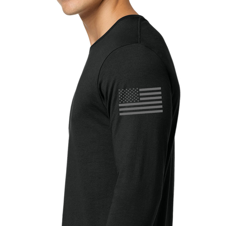 A man wearing a black long-sleeve shirt with a dark gray American flag graphic printed on the upper left sleeve, shown in a side profile view against a plain white background. #color_black