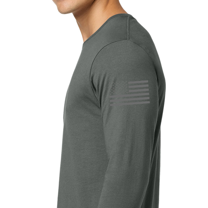 A man wearing a dark gray long-sleeve athletic shirt, shown in a side profile against a plain white background. A subtle, tonal American flag graphic is printed on the upper left sleeve. #color_charcoal