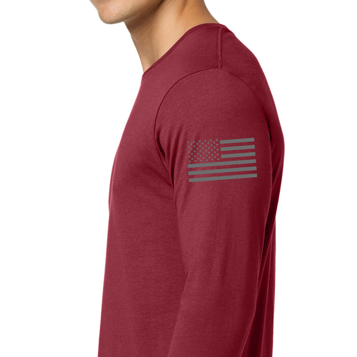 A man wearing a heathered burgundy long-sleeve t-shirt with a dark gray distressed American flag graphic printed on the upper left sleeve, shown in a side profile view against a plain white background. #color_cardinal-red