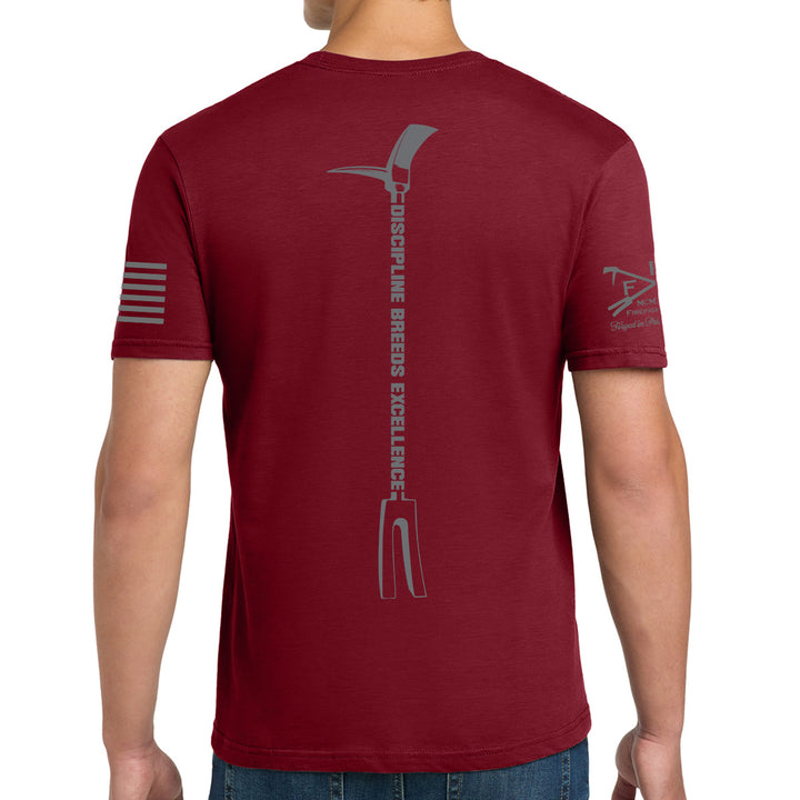 A man wearing a maroon short-sleeve t-shirt, viewed from the back. The shirt features a large gray vertical graphic of a pitchfork with the text 'DISCIPLINE BREEDS EXCELLENCE' down the center, a gray flag design on the right sleeve, and a small gray logo on the left sleeve. #color_cardinal-red