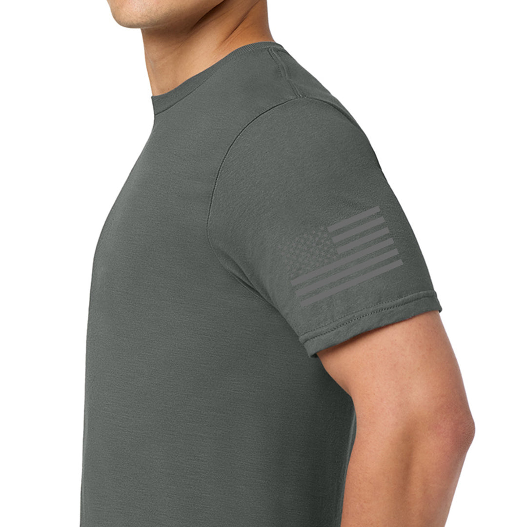 A man wearing a dark gray crewneck t-shirt, shown from the side. The t-shirt features a subtle, tonal American flag graphic printed on the left sleeve. #color_charcoal