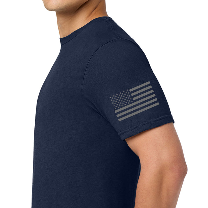 A man wearing a navy blue short-sleeve t-shirt with a distressed gray American flag graphic printed on the left sleeve, shown in a side-profile view against a white background. #color_navy