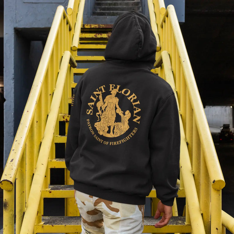 A man wearing a black firefighter hoodies shirt with a full back design featuring the Saint Florian Patron Saint of Firefighters