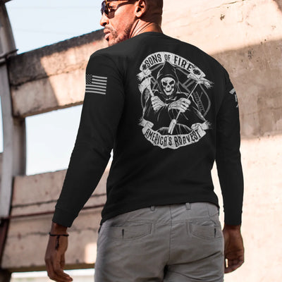 A man wearing a firefighter graphic long sleeve shirt featuring a skeleton holding a hooligan bar and an axe with text Sons Of Fire Americas Bravest