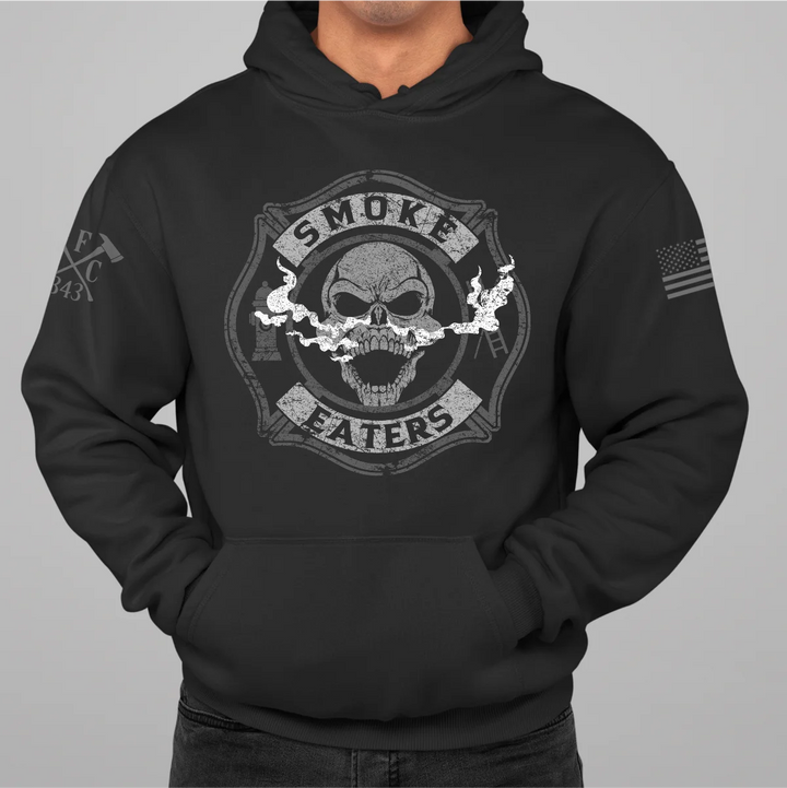 Front view of firefighter hoodies in black color featuring a full-front design print of a skull inhaling smoke, with a distressed grey and off-white look. 