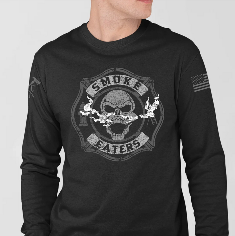 a man wearing a black firefighter long sleeves in black color featuring full-front design of a skull inhaling smoke, with a distressed grey and off-white look. 