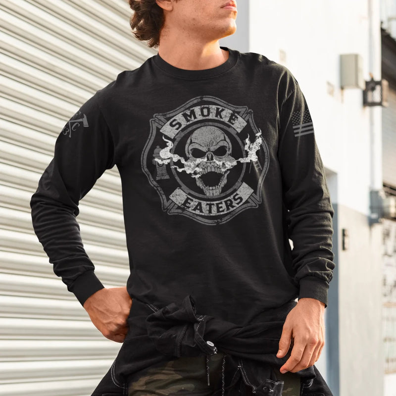 a man wearing a black firefighter long sleeves in black color featuring full-front design of a skull inhaling smoke, with a distressed grey and off-white look. 