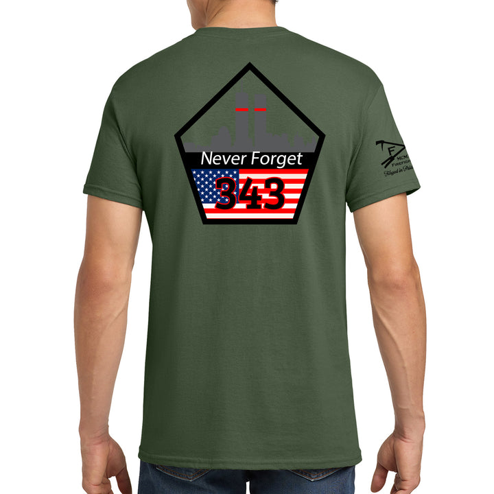 A man wearing an olive green t-shirt, viewed from the back. The shirt features a large graphic on the back with a black pentagonal outline, the words 'Never Forget' in white, the number '943' in red over an American flag design, and a small black graphic on the left sleeve. #color_military-green