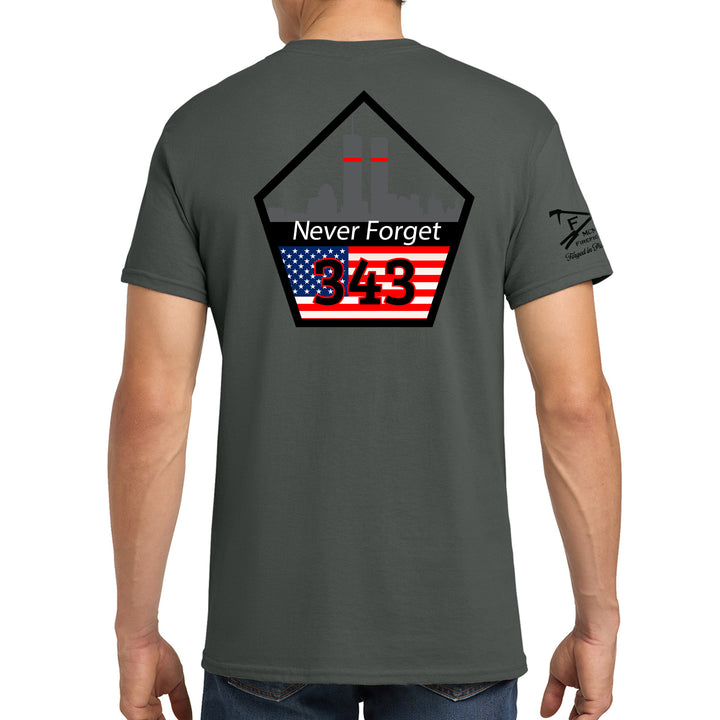 A man wearing a dark gray t-shirt, viewed from the back. The shirt features a large graphic on the back with a black pentagon outline, the words 'Never Forget' in white, a stylized American flag with red and white stripes and a blue canton, and the number '343' in red. #color_charcoal